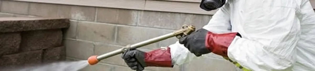Pest control technician applying exterior insect treatment along a home foundation in Denver, CO
