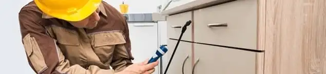 Roach exterminator applying treatment under kitchen cabinets in Denver, CO
