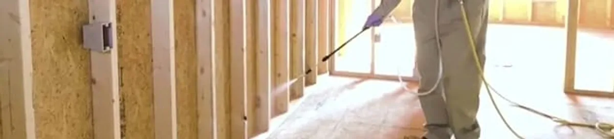 Termite treatment technician applying spray along framing and unfinished walls in Denver, CO